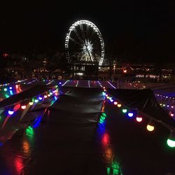 Illuminated ferris wheel against sky in city at night