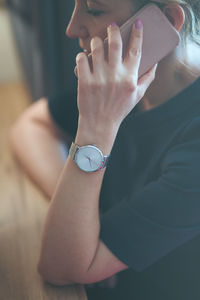 Side view of mature woman talking on smart phone while sitting by table at home