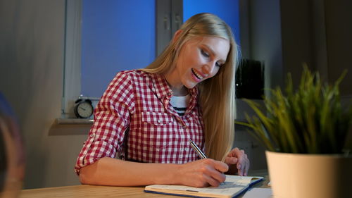 Smiling young woman writing in book while sitting at table