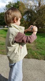Side view of boy photographing with camera on footpath