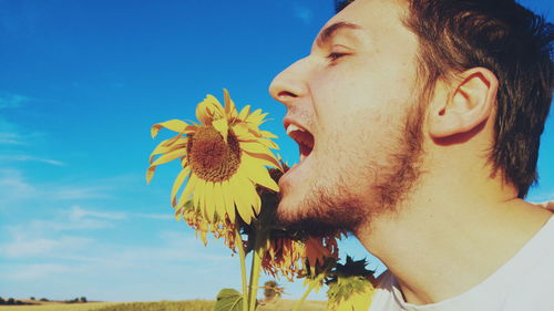 Close-up of mid adult man holding sunflower against blue sky during sunny day