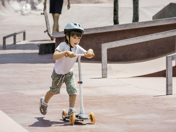  boy rides kick scooter in skate park. concrete bowl structures in urban park. training to skate.