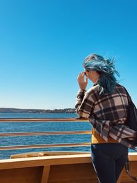 Rear view of woman standing at beach against clear blue sky