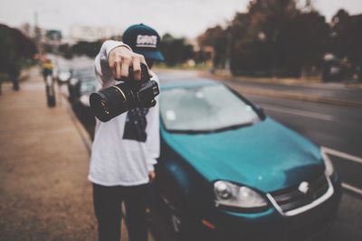 Man holding camera while standing on sidewalk