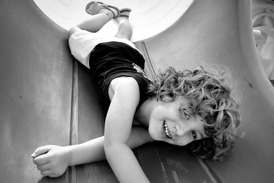 Full length portrait of smiling boy lying on slide at playground