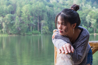 Thoughtful woman standing by railing against lake in forest