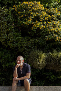 Young man looking away while sitting on tree