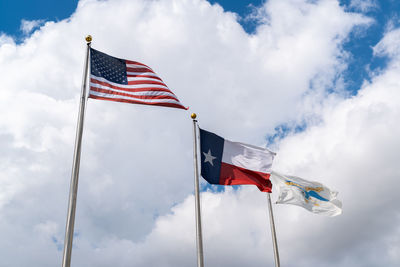 Low angle view of flags waving against cloudy sky