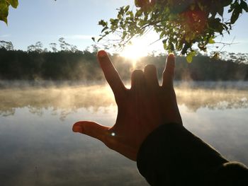 Close-up of hand holding sun over lake