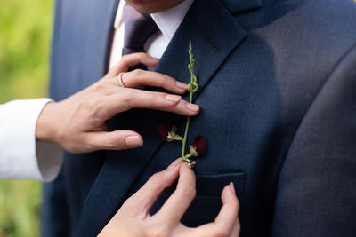 Cropped hands of woman adjusting boutonniere of bridegroom