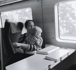 Mother carrying daughter while sitting in train