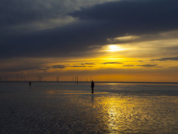 Silhouette people standing on beach against sky during sunset