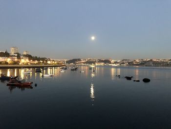 Illuminated city by river against sky