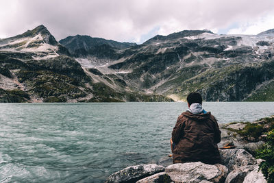 Rear view of woman sitting on snowcapped mountain against sky