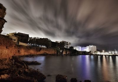 Illuminated buildings by sea against sky at dusk