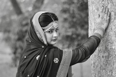 Portrait of young woman wearing sari by tree trunk