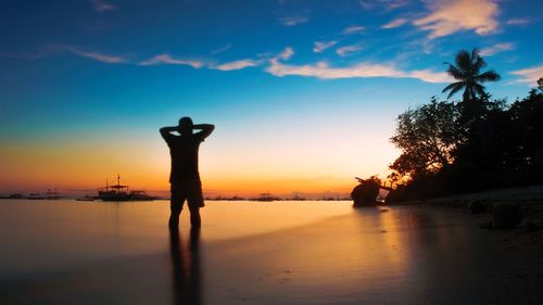 Silhouette man standing on beach against sky during sunset