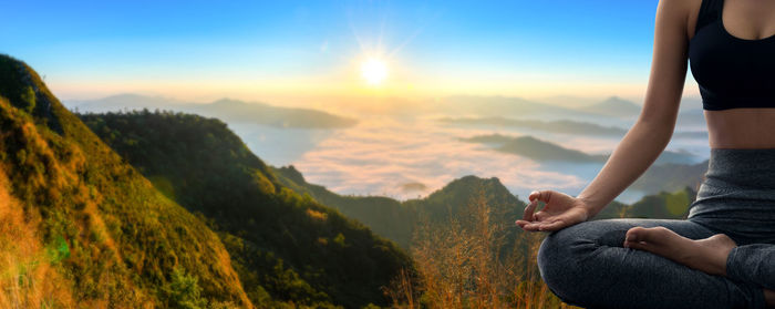 Rear view of woman doing yoga on mountain against sky during sunset