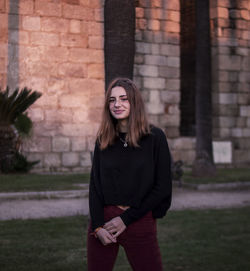 Portrait of young woman standing against brick wall