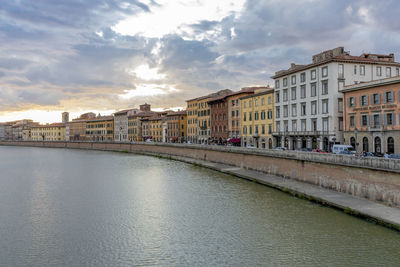 View of buildings by river against cloudy sky