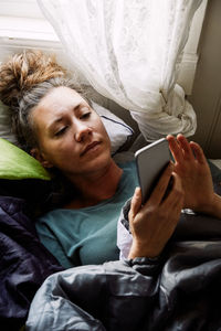 High angle view of mid adult woman using smart phone while lying on bed in cottage