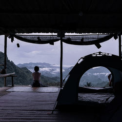 Rear view of woman sitting on a hut overlooking sunrise clouds