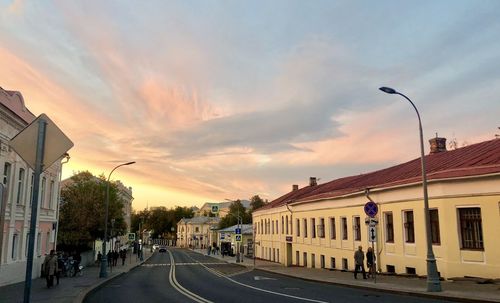 Road by buildings against sky during sunset