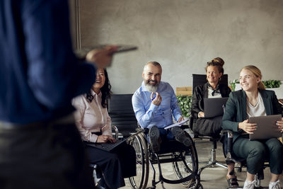 Smiling male and female colleagues looking at businessman during meeting