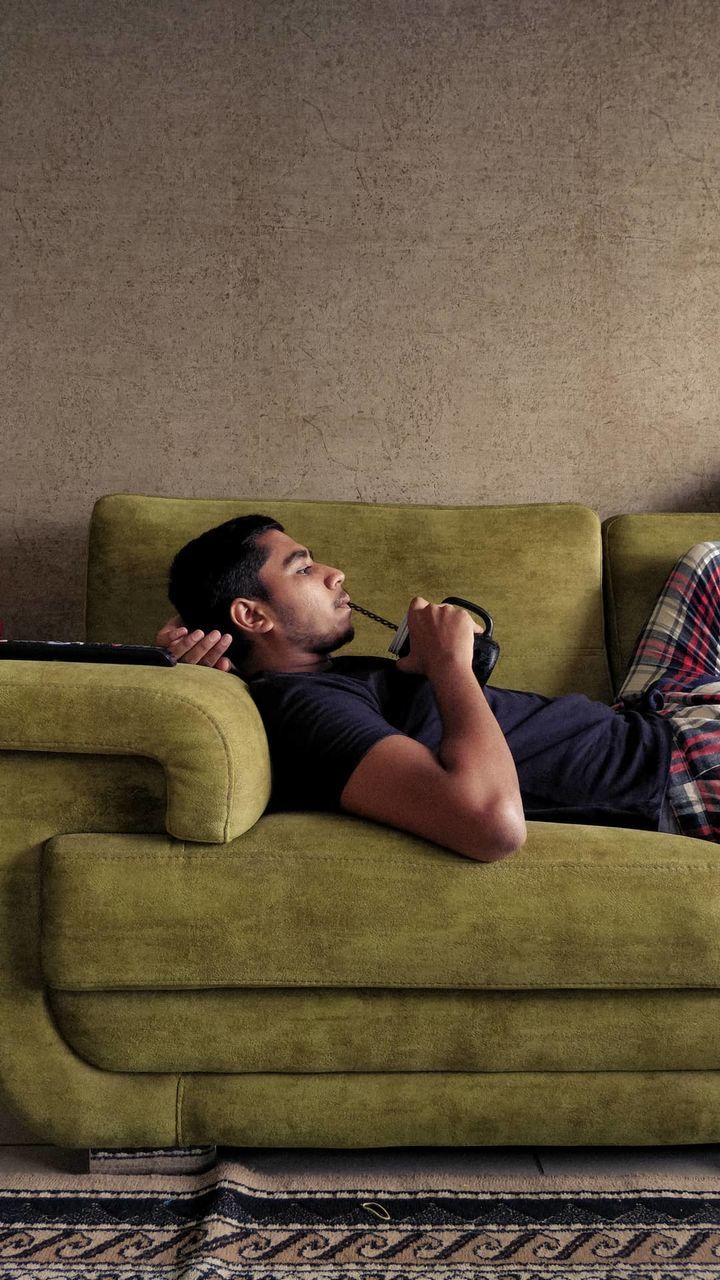 relaxation, sofa, furniture, sitting, couch, one person, indoors, adult, lifestyles, sofa bed, domestic room, lying down, living room, person, full length, leisure activity, young adult, men, casual clothing, studio couch, comfortable, home interior, domestic life, women, resting, clothing, copy space, side view, looking, limb, eyes closed, tired