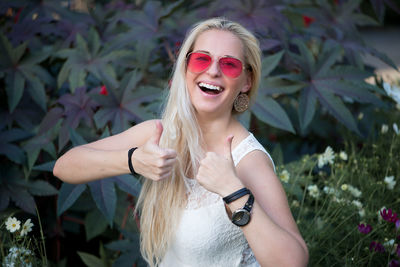 Portrait of beautiful woman gesturing thumbs up while standing against plants