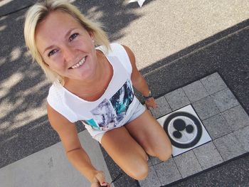 High angle portrait of smiling young woman sitting on footpath