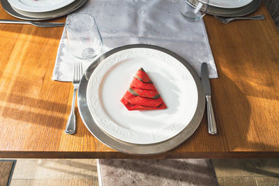 Red christmas napkin on clean porcelain dinner plate. high angle view.