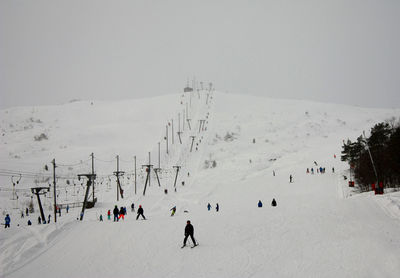 People skiing on snow covered hill against clear sky