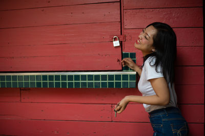 Side view of a smiling young woman standing against red wall