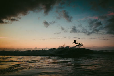 Silhouette man surfing in lake against sky during sunset