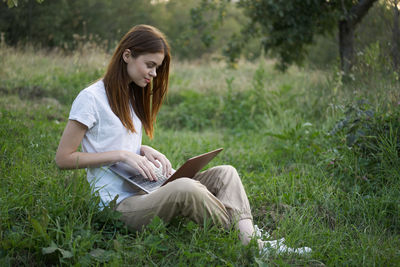 Young woman using laptop while sitting on field