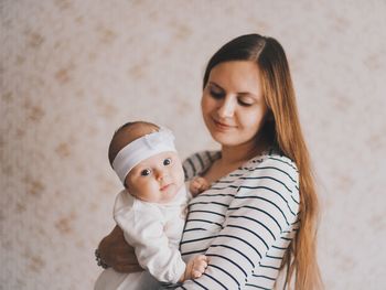 Smiling woman carrying baby girl while standing against wall at home