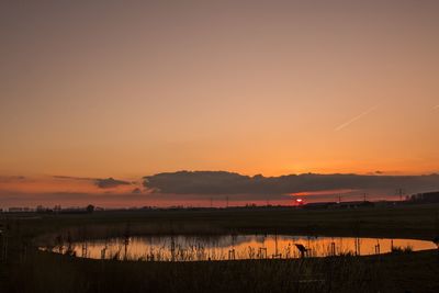 Scenic view of lake amidst field against sky during sunset