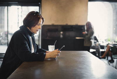 Side view of senior woman using smart phone at cafe