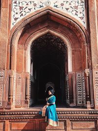 Woman wearing hijab sitting against historic building