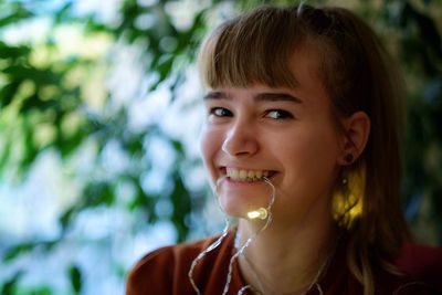 Close-up portrait of smiling teenage girl carrying illuminated string light in mouth
