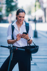 Full length of a smiling young woman using phone in city