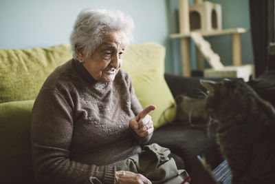 Senior woman sitting on the couch scolding her cat