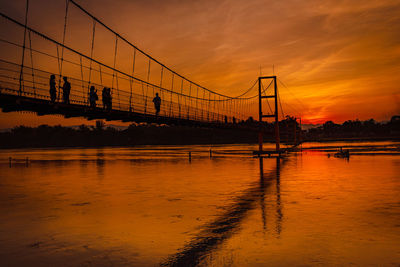 Silhouette bridge over river against sky during sunset