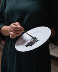 Midsection of woman holding paintbrush and plate