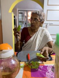 Senior woman holding fruit while sitting on table at home