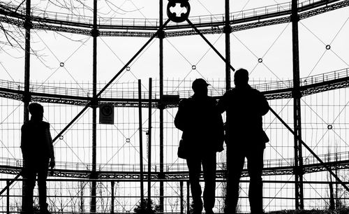Silhouette people standing at gasometer 