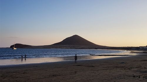 Silhouette people at beach against clear sky during sunset