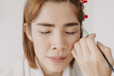 Close-up of young woman applying make-up against white background