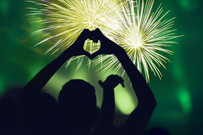 Silhouette man making heart shape against firework display at night